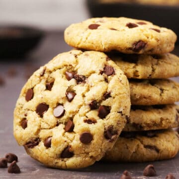 Gluten free chocolate chip cookie leaning against a stack of cookies.