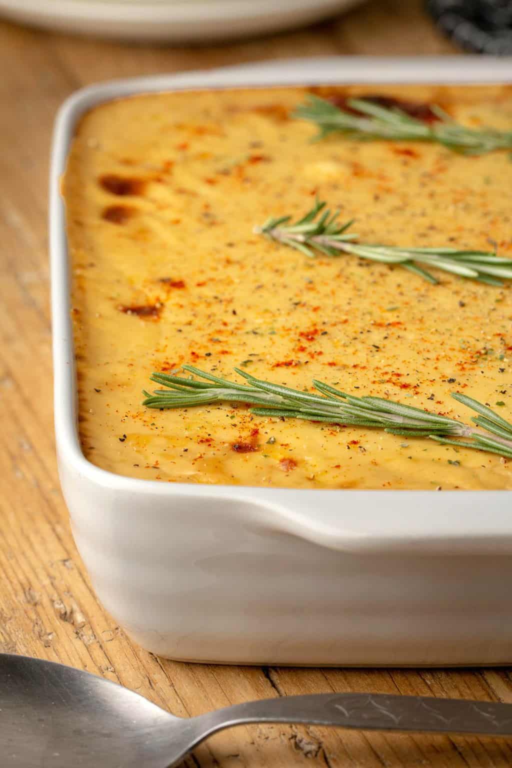 Vegan moussaka topped with fresh rosemary in a white baking dish. 