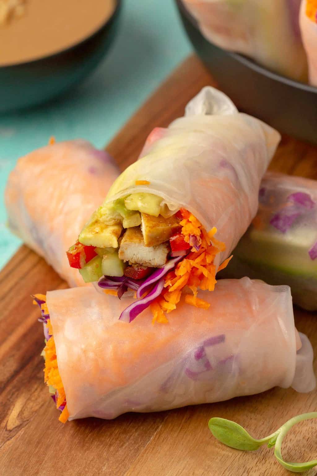 Vegan summer rolls stacked up on a wooden board. 