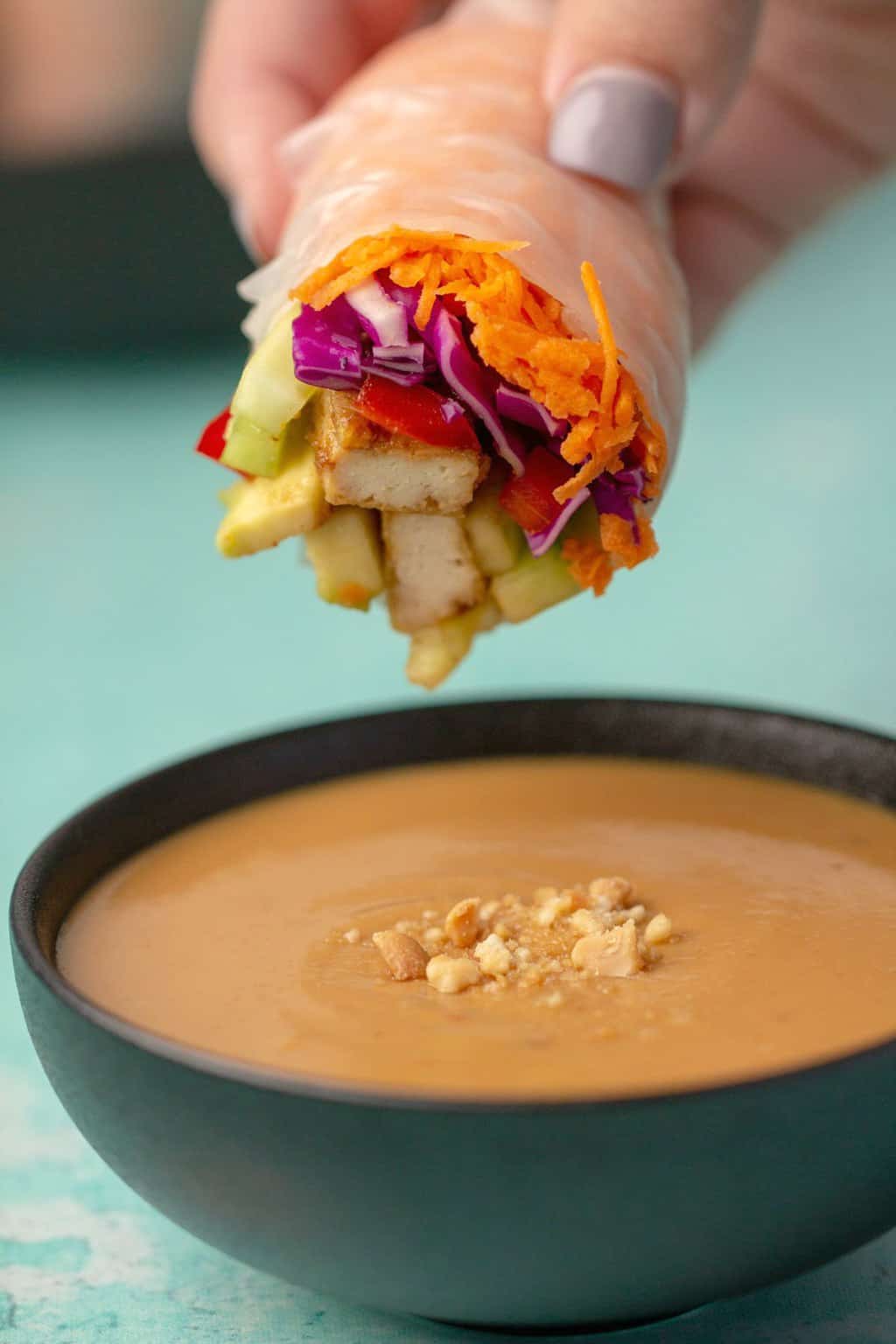 Vegan summer roll about to dip into a bowl of peanut sauce. 