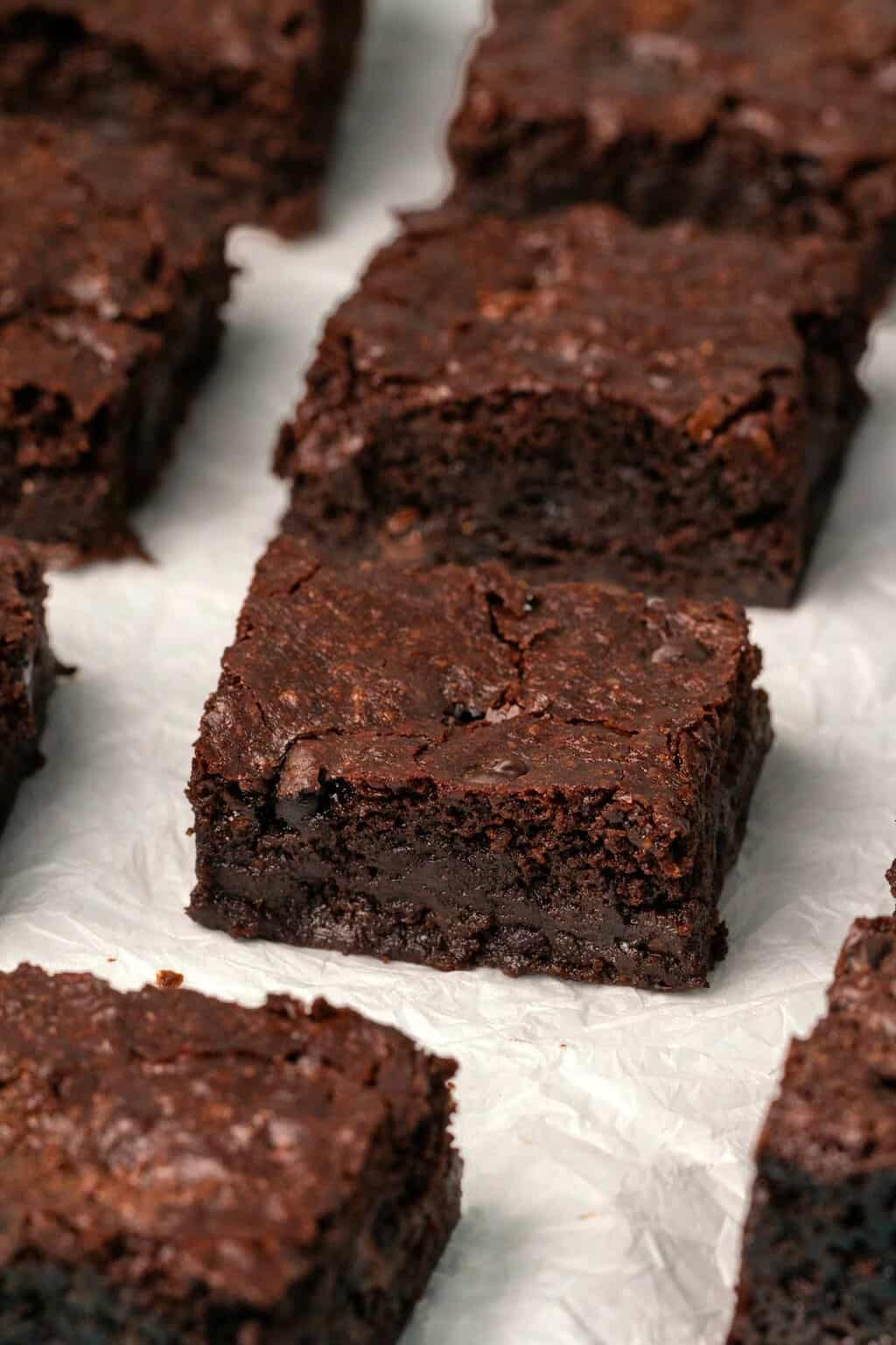 Vegan gluten free brownies cut into squares on parchment paper. 