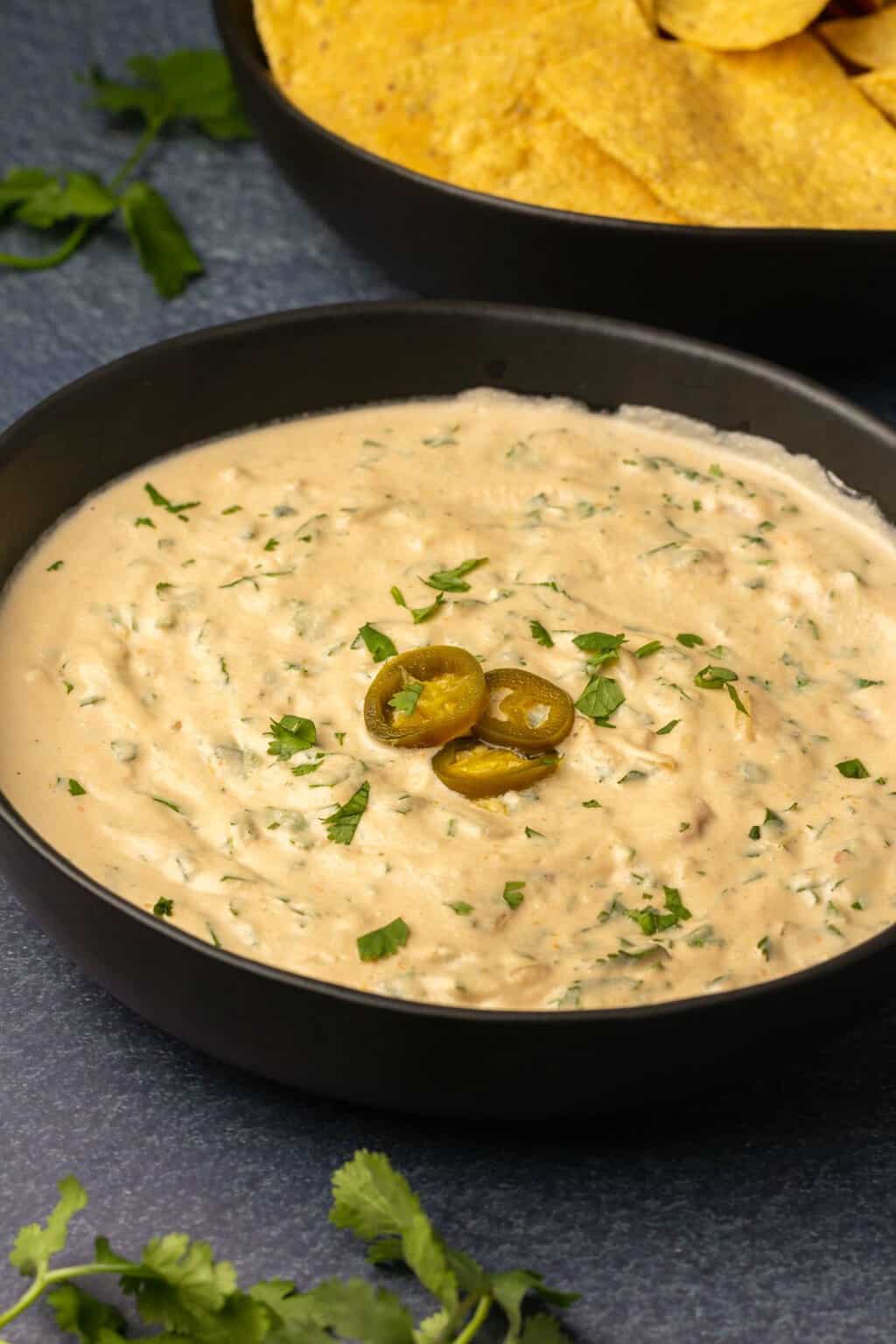 Cashew queso topped with sliced jalapeños in a black bowl. 