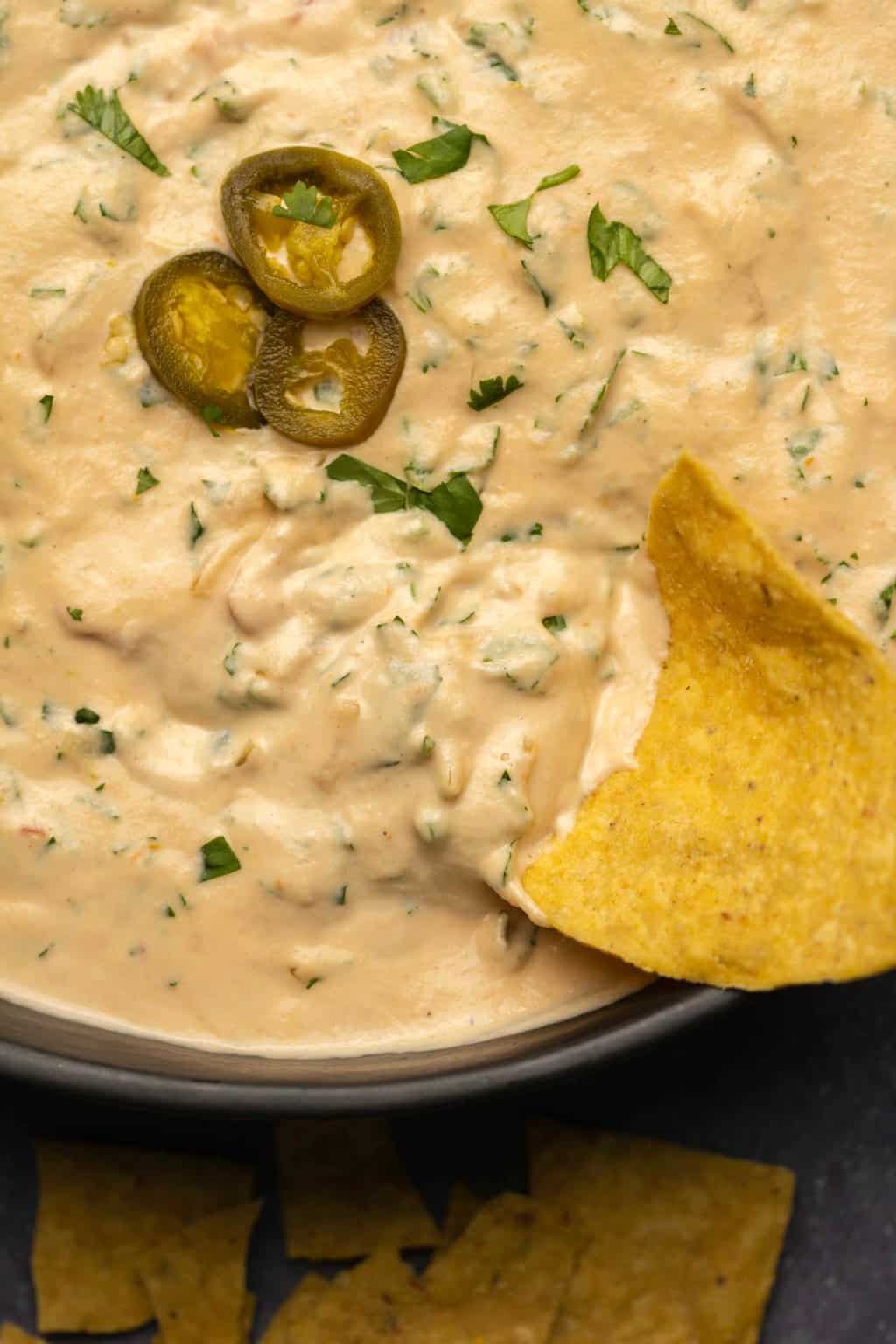Tortilla chip dipping into a bowl of cashew queso with chopped cilantro. 