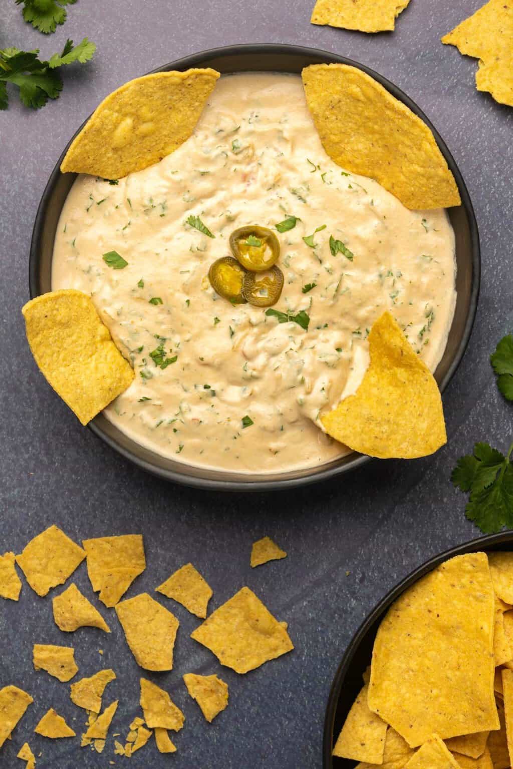 Cashew queso topped with sliced jalapeños and tortilla chips in a black bowl. 