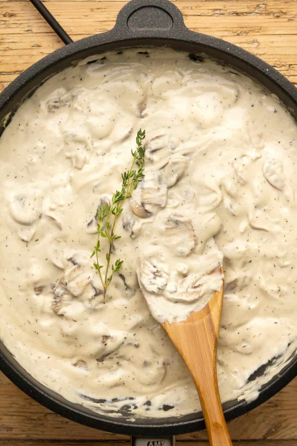 Vegan mushroom sauce topped with a sprig of fresh thyme in a frying pan. 