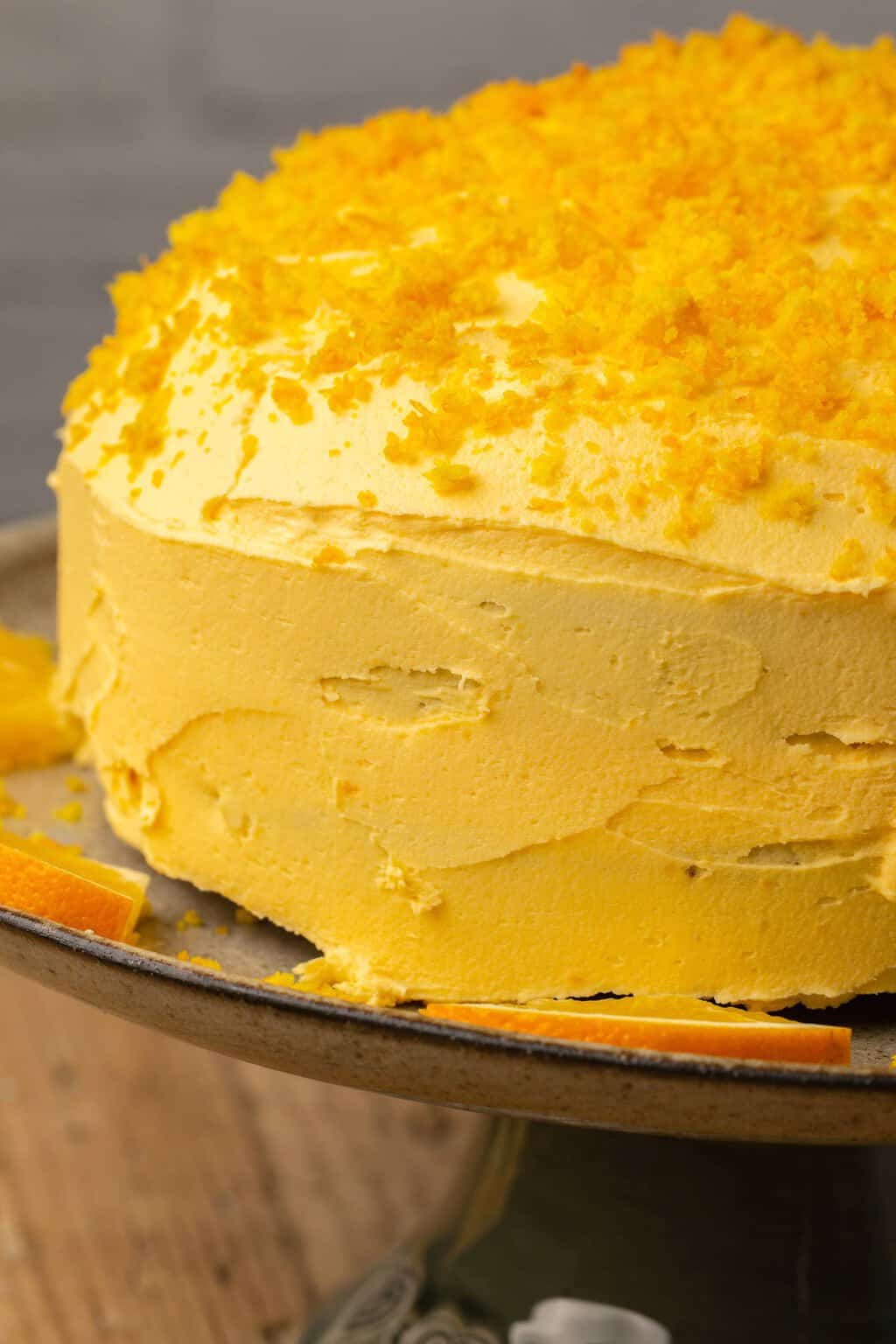 Vegan orange cake topped with orange zest on a cake stand. 