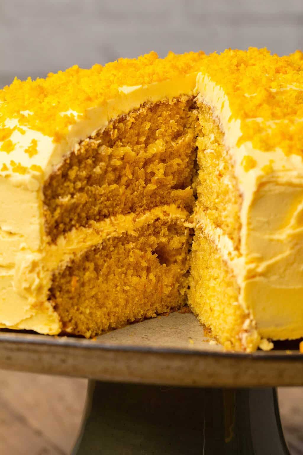 Vegan orange cake on a cake stand with one slice missing. 