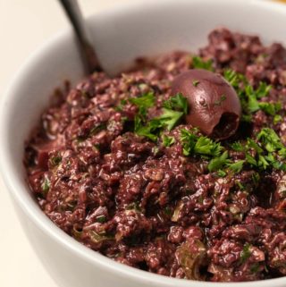 Olive tapenade in a white bowl with a spoon.
