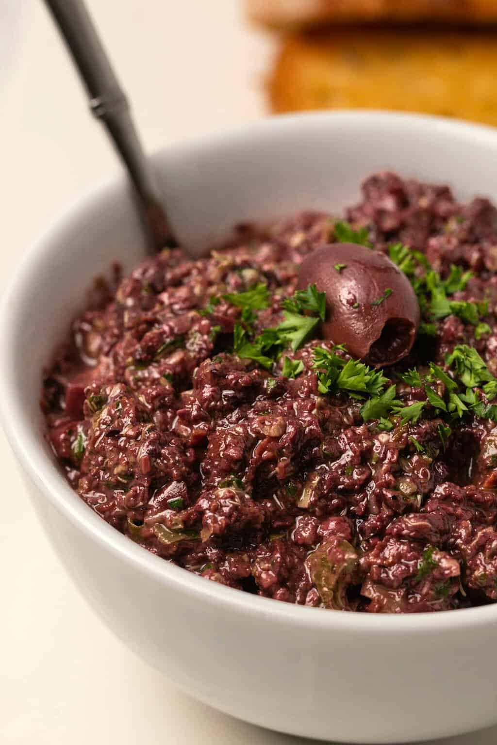 Olive tapenade in a white bowl with a spoon. 