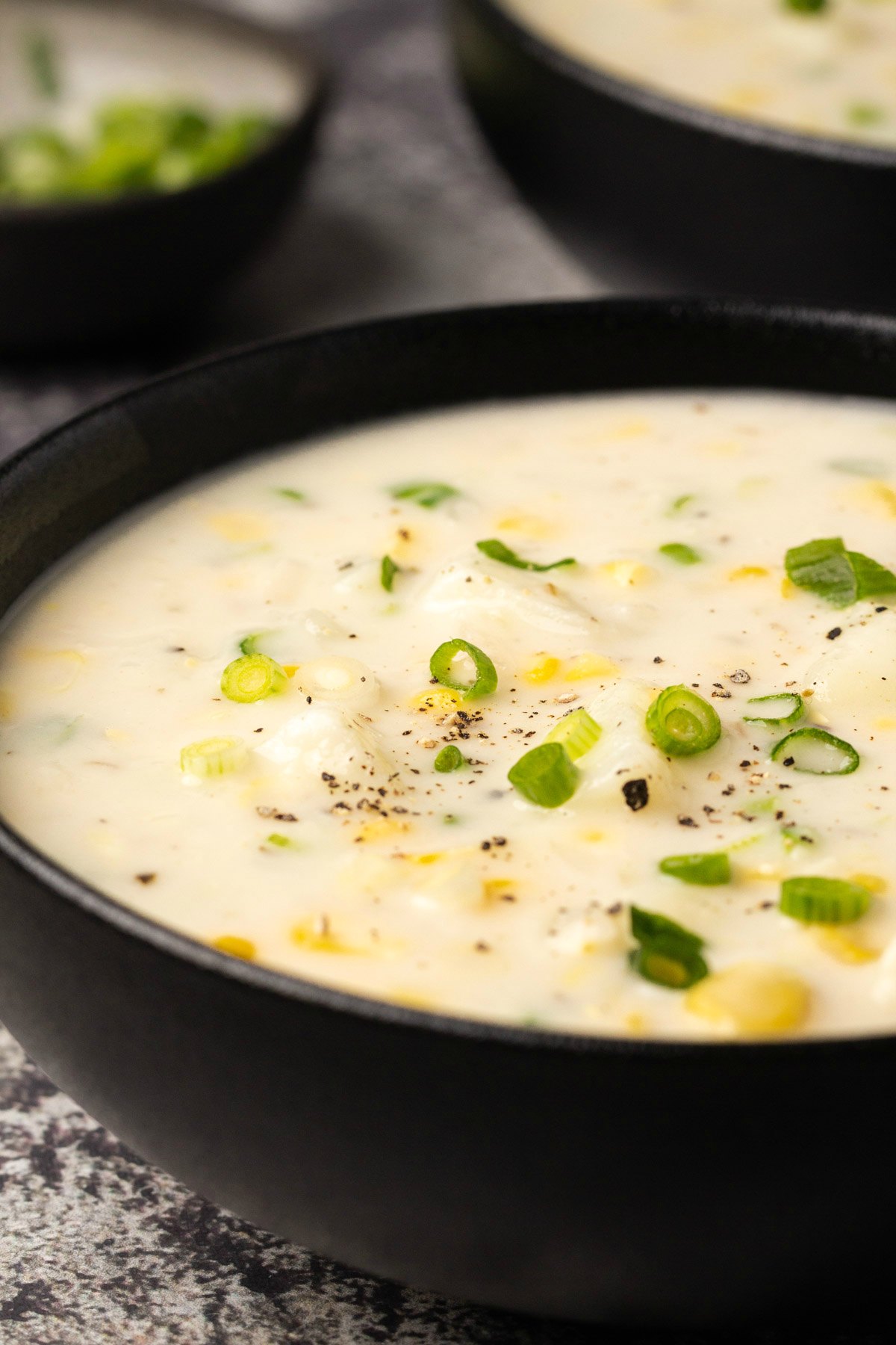 Vegan corn chowder topped with chopped spring onions in a black bowl. 
