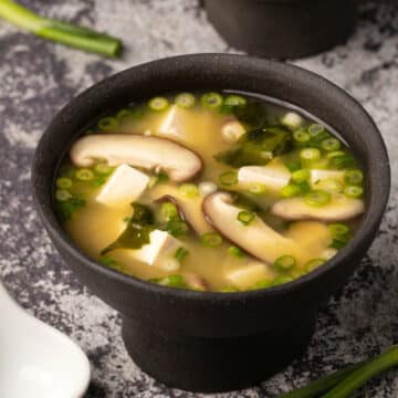 Vegan miso soup in a black bowl.