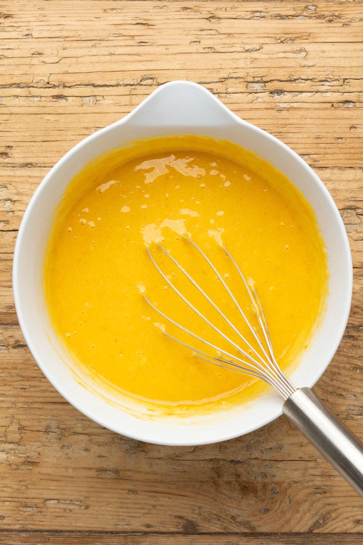 Orange cake batter in a mixing bowl with a whisk. 