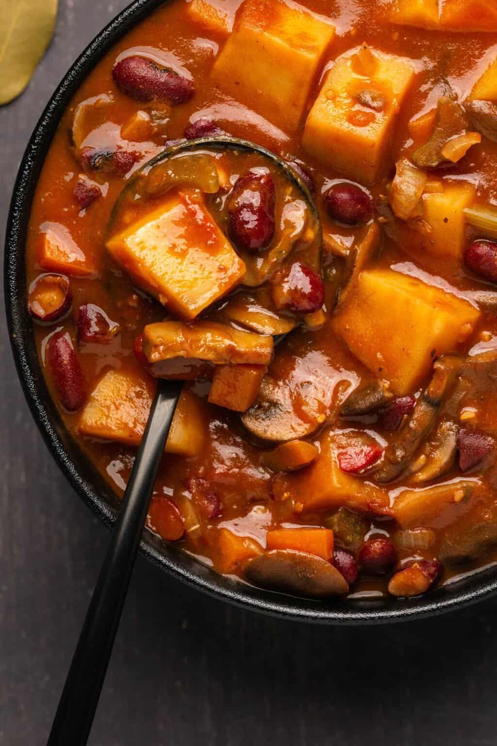 Vegan stew in a black bowl with a spoon. 