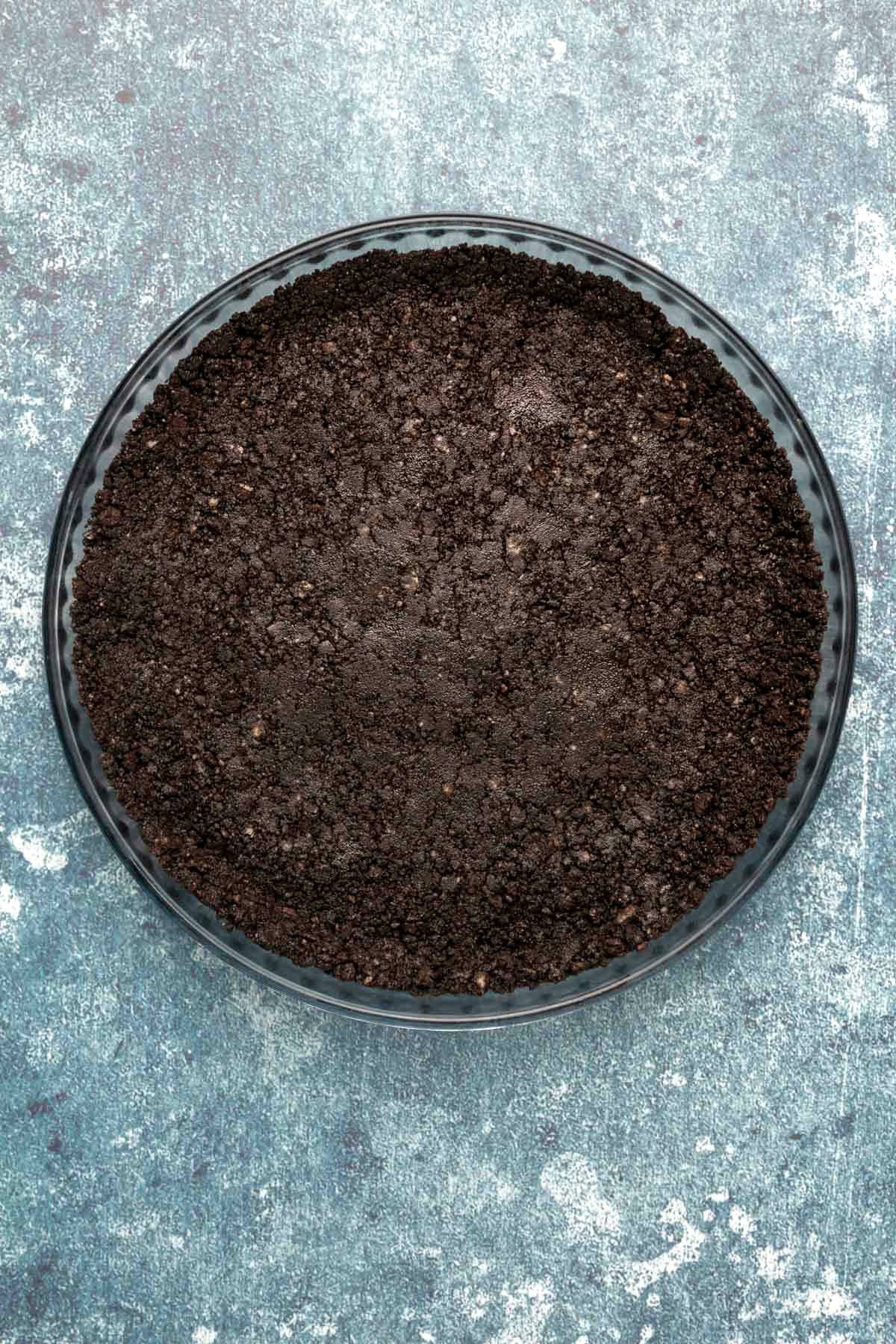 Oreo cookie crust pressed down into a glass pie dish.