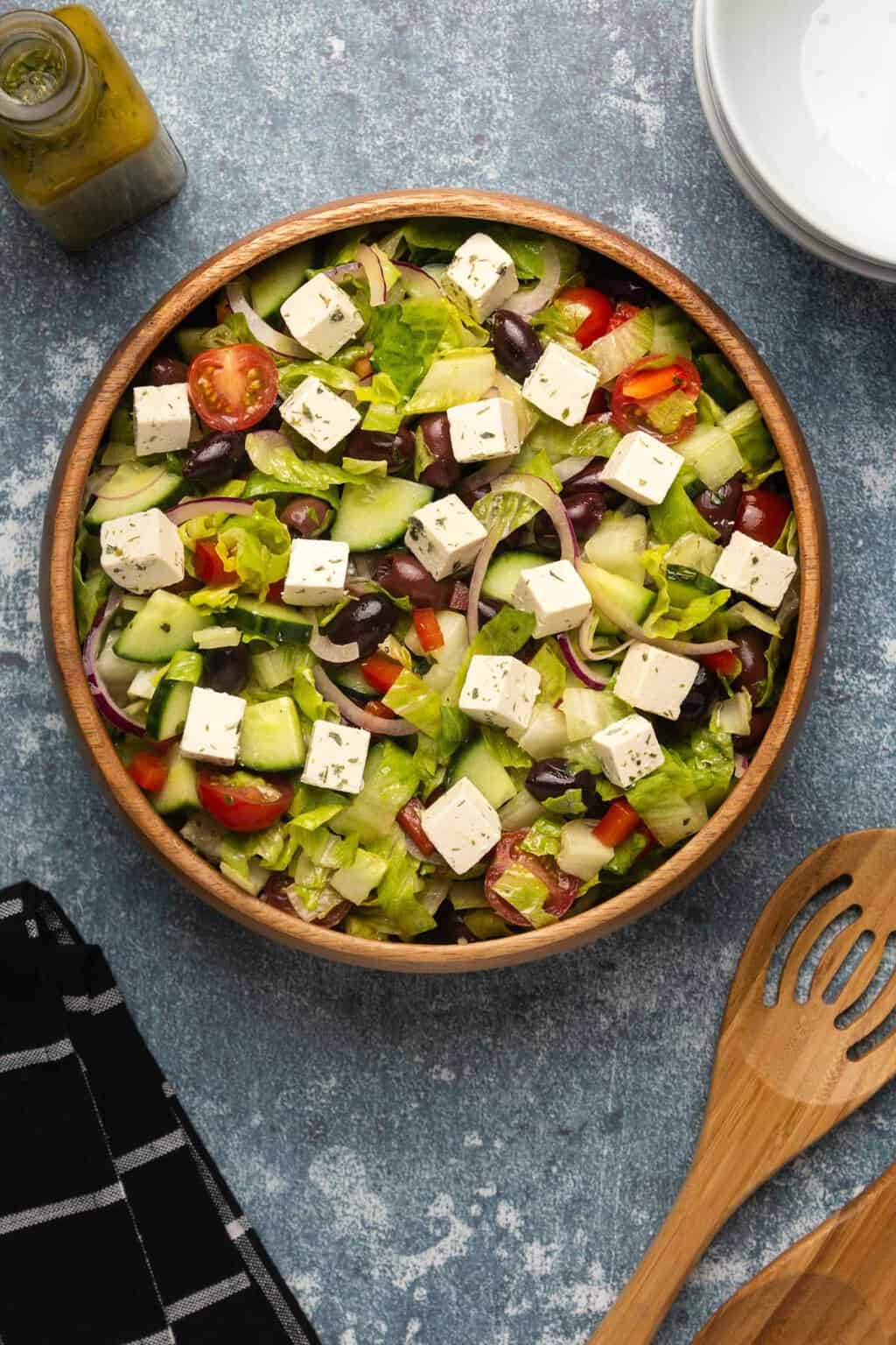 Vegan Greek salad topped with vegan feta in a wooden salad bowl. 