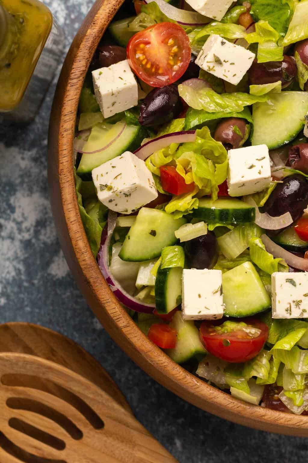 Vegan Greek Salad topped with vegan feta in a wooden salad bowl. 