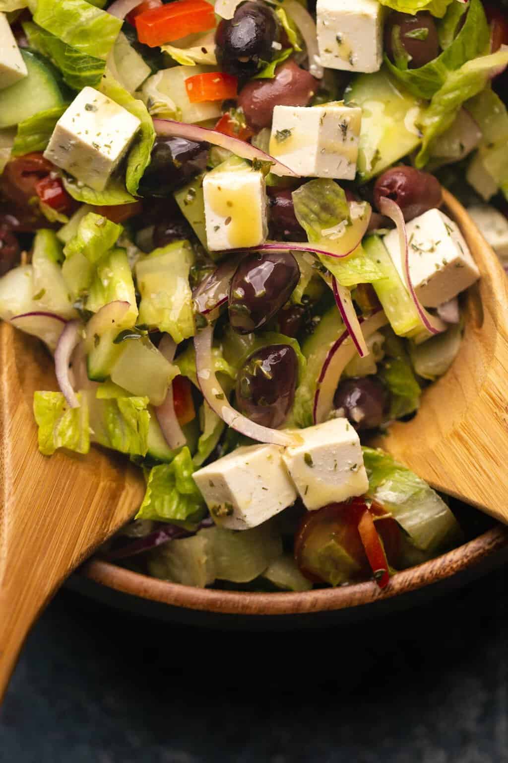Vegan Greek Salad topped with vegan feta and vinaigrette in a wooden salad bowl. 