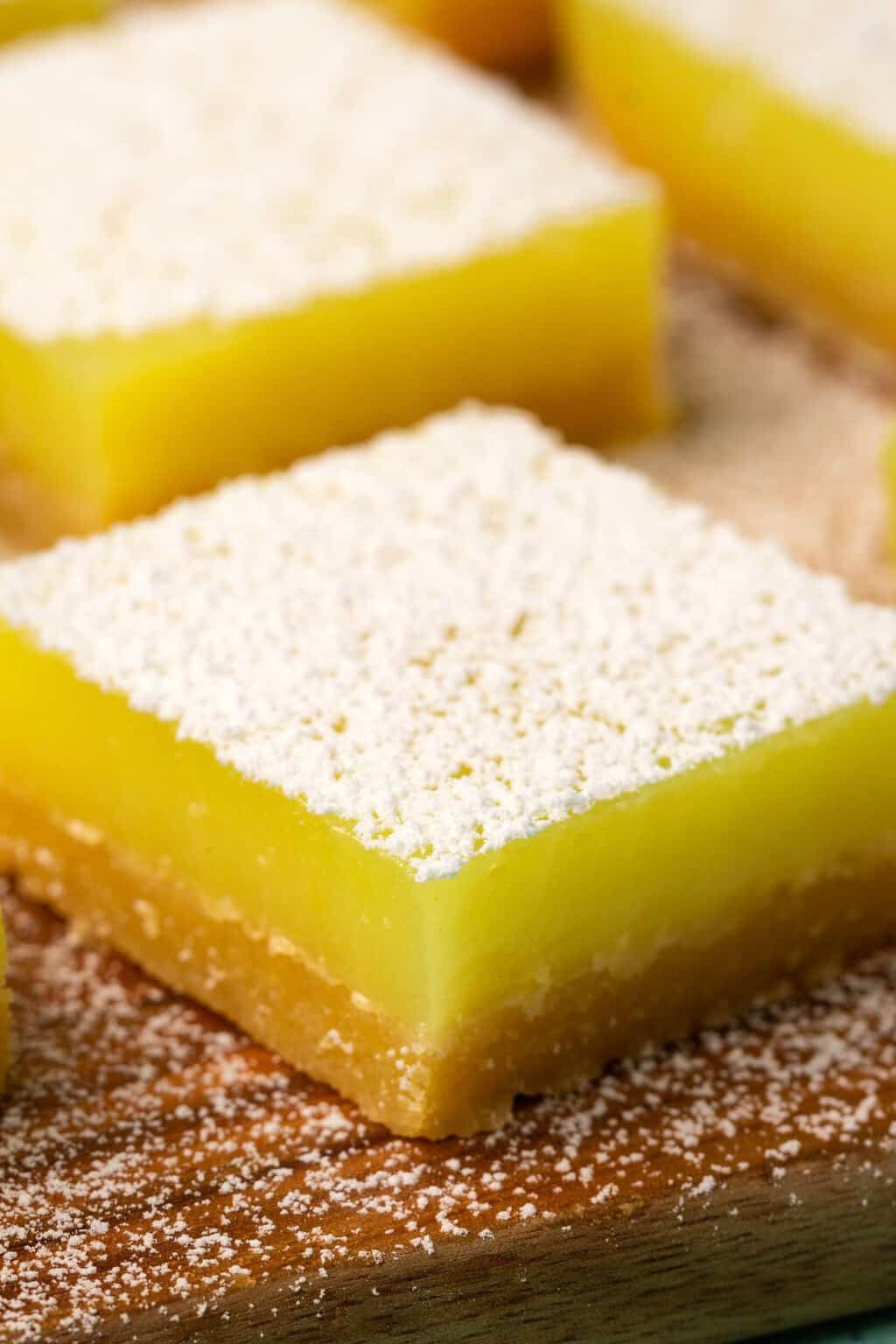 Vegan lemon bars topped with powdered sugar on a wooden board. 