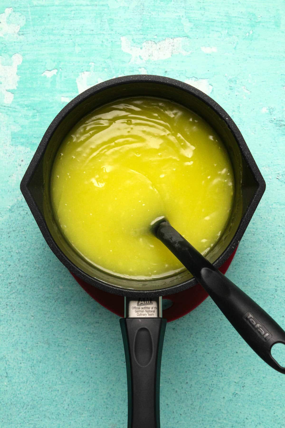 Vegan lemon filling in a saucepan with a spoon.