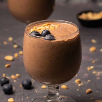 Vegan protein shake in a glass topped with crushed peanuts and blueberries.