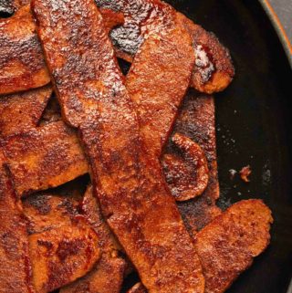 Vegan bacon strips in a frying pan.