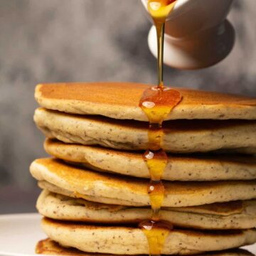 Vegan gluten free pancakes in a stack on a white plate with syrup drizzling over the top.
