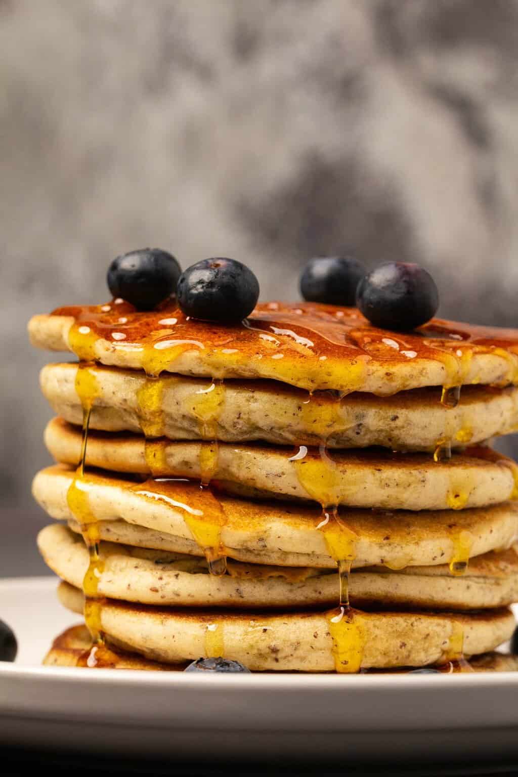 A stack of vegan gluten free pancakes with syrup and blueberries. 