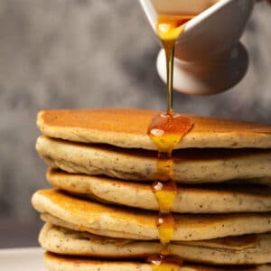 Syrup pouring over a stack of pancakes.