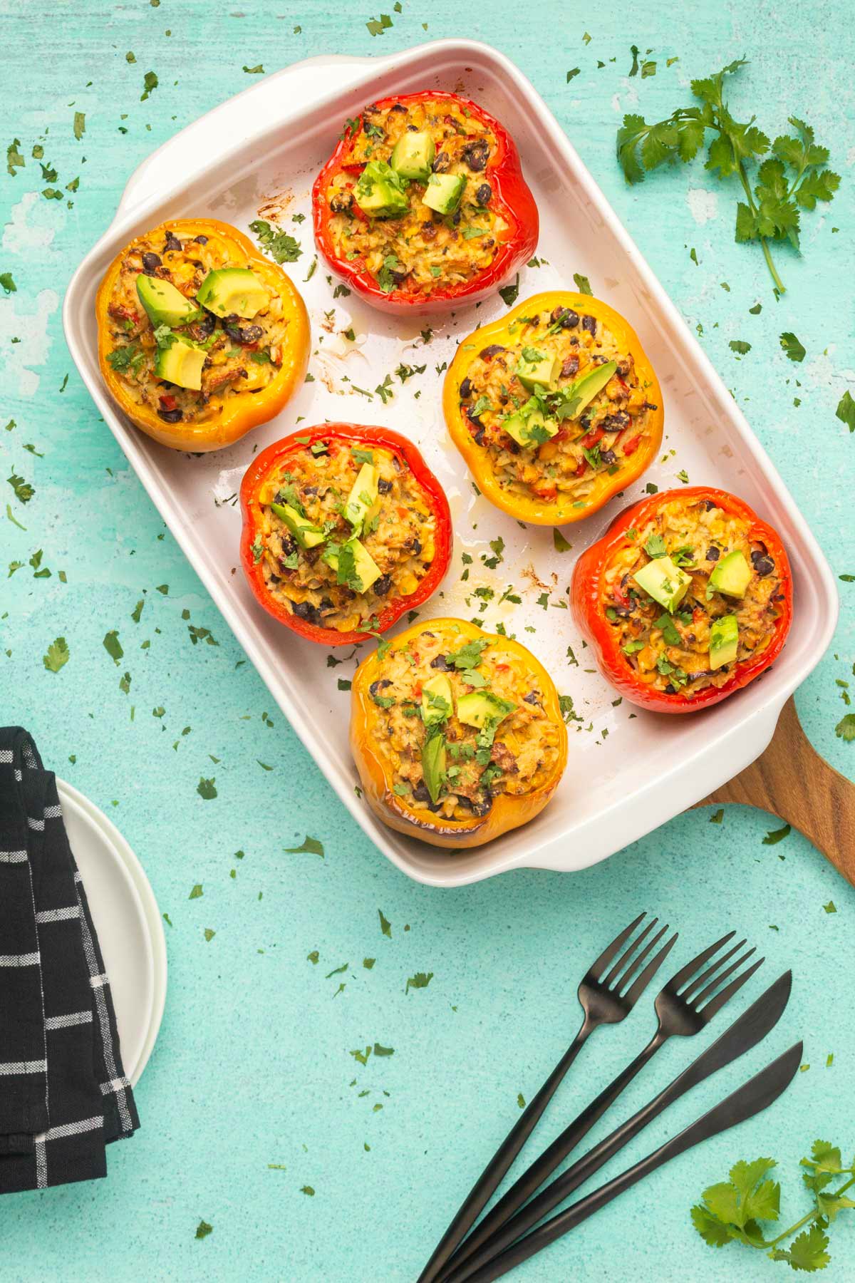 Vegan stuffed peppers topped with chopped avocado and cilantro in a white dish. 