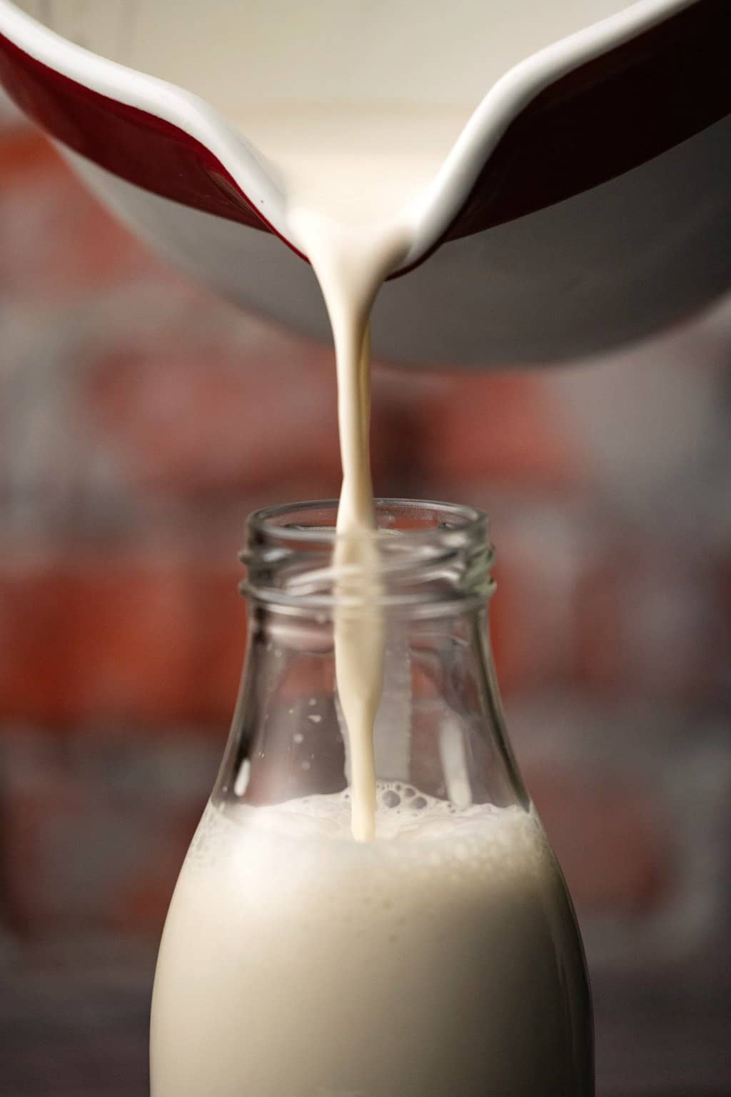 Pouring almond milk into a glass milk bottle. 