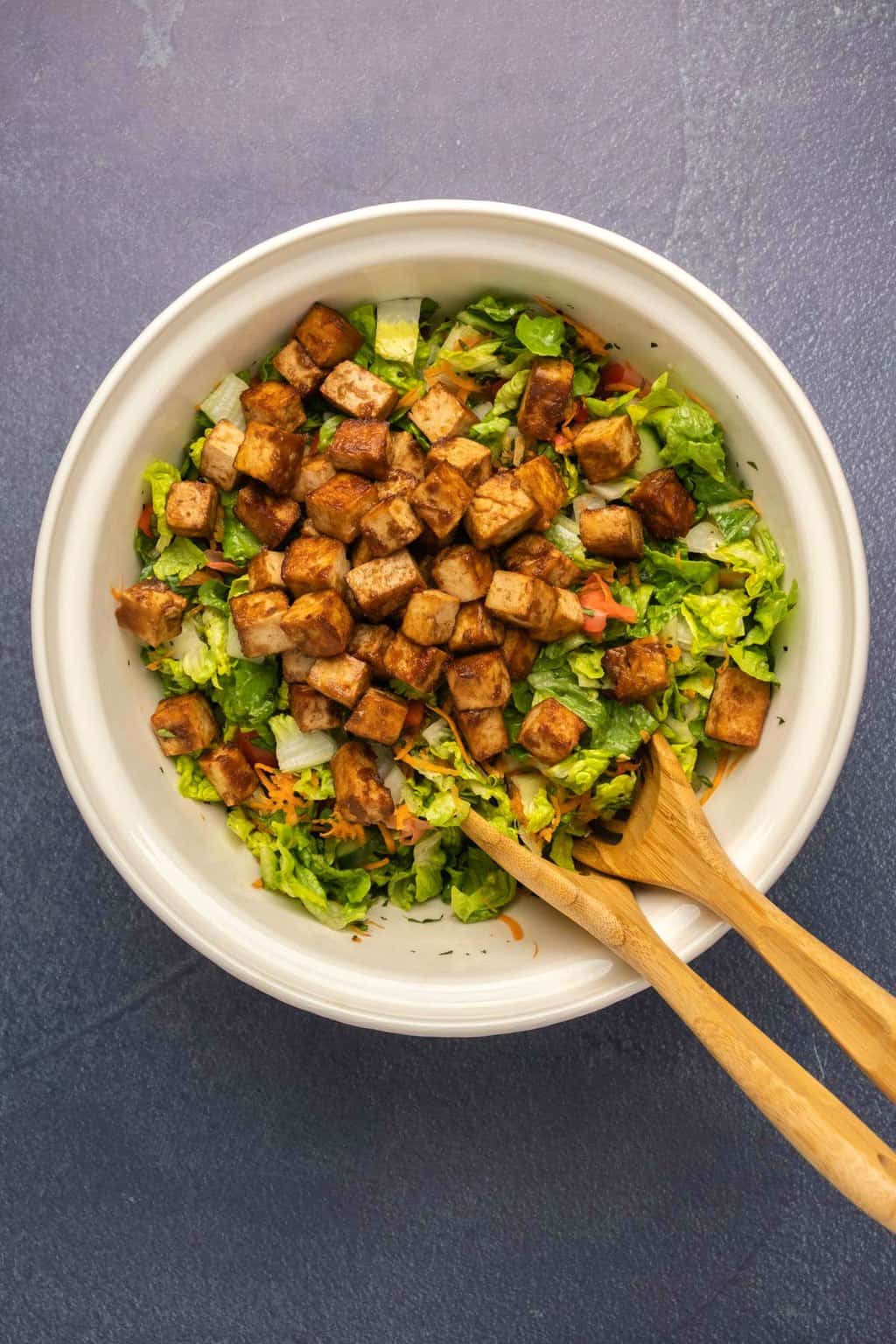 Marinated tofu on top of a salad in a mixing bowl. 