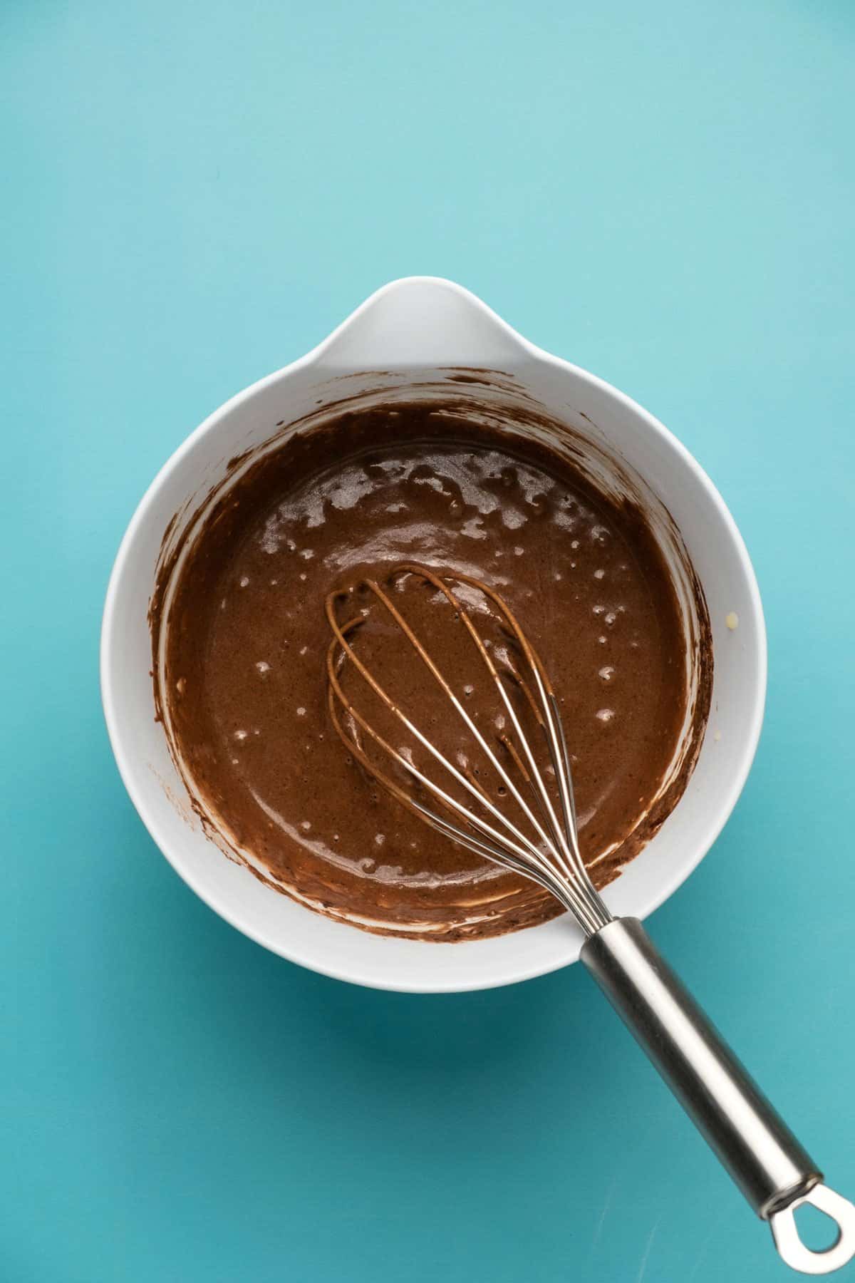 Batter for chocolate donuts in a mixing bowl with a whisk.