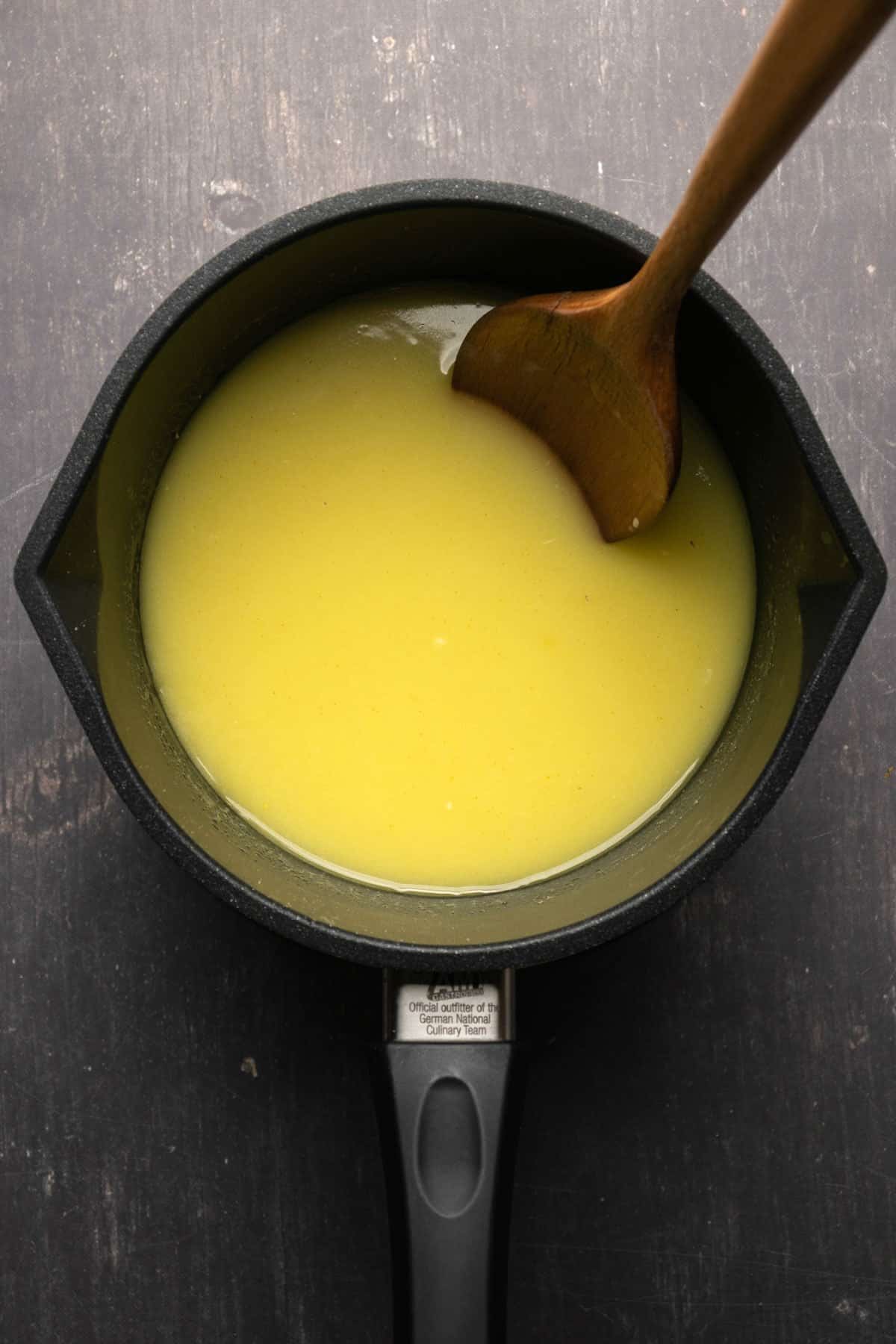Lemon curd mix in a saucepan with a wooden spoon.