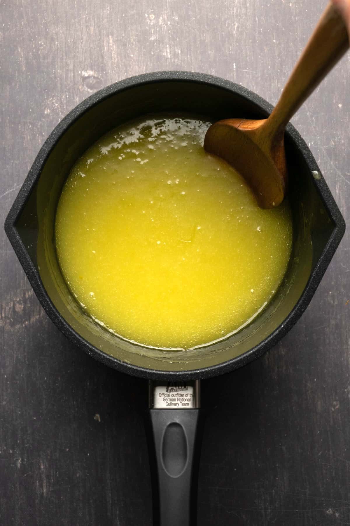 Vegan lemon curd in a saucepan with a wooden spoon.