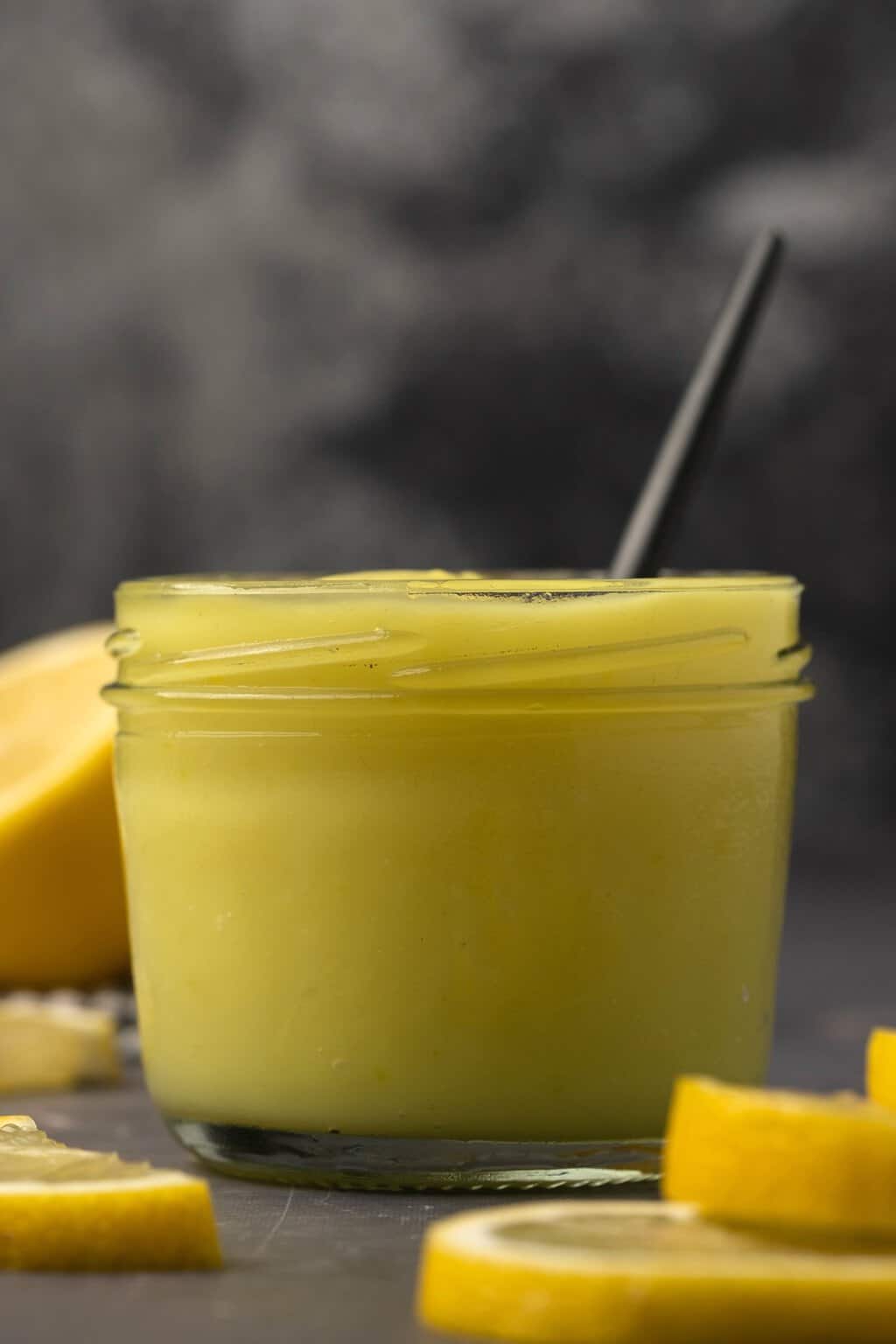 Vegan lemon curd in a glass jar with a spoon. 