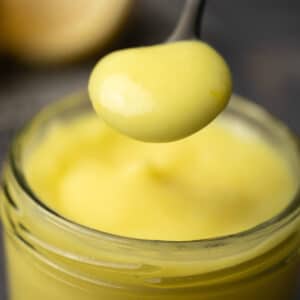 Vegan lemon curd in a glass jar with a spoon.