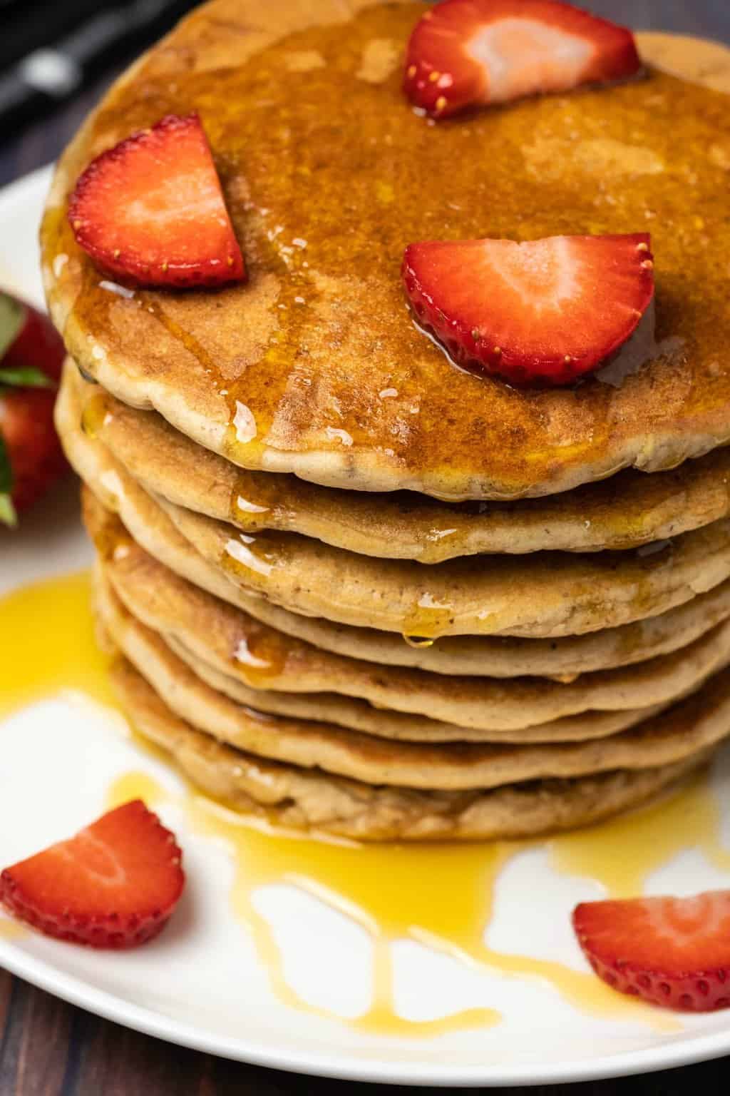 A stack of vegan pancakes topped with fresh strawberries and syrup. 