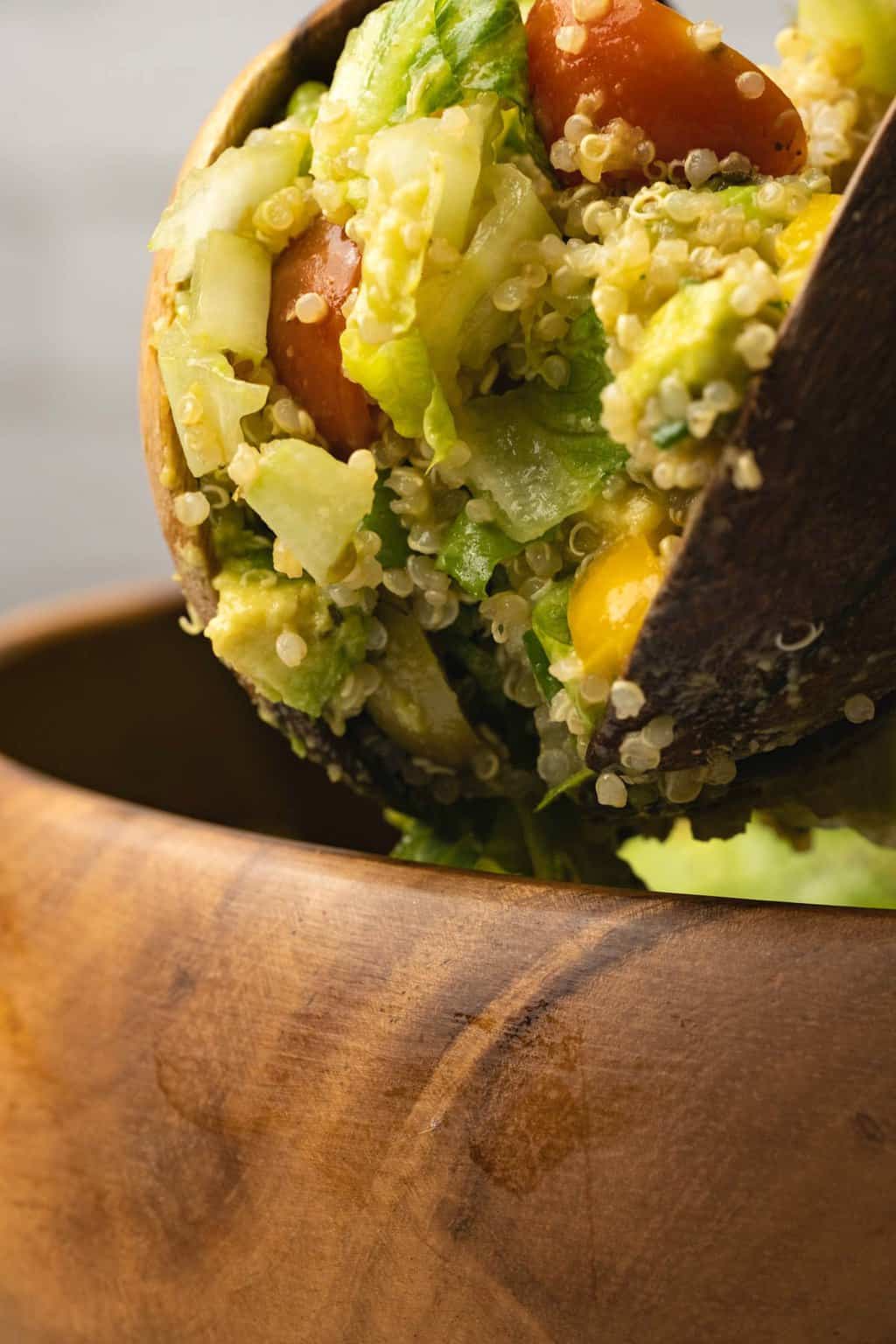 Vegan quinoa salad lifting out of a salad bowl with wooden salad spoons. 