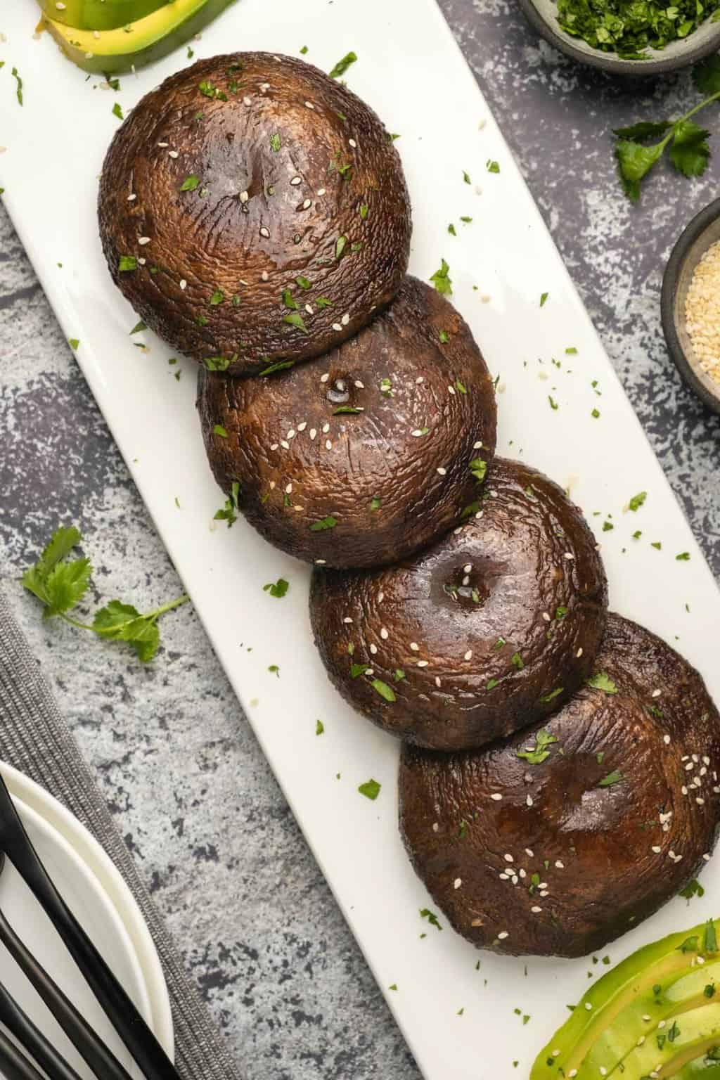 Baked portobello mushrooms sprinkled with chopped cilantro and sesame seeds on a white plate.