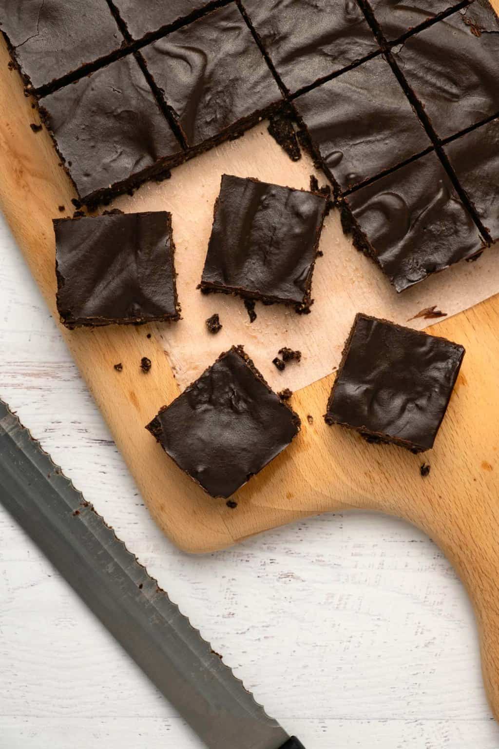 Raw vegan brownies cut into squares on a wooden cutting board. 
