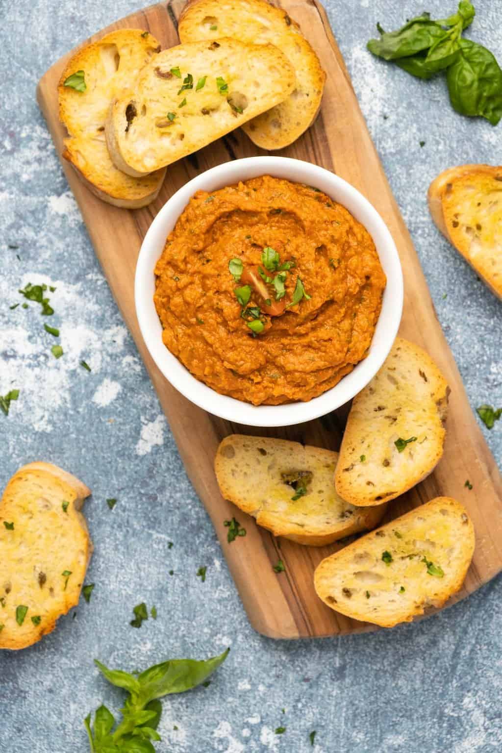 Sun dried tomato pesto in a white bowl with toasted bread on the sides. 