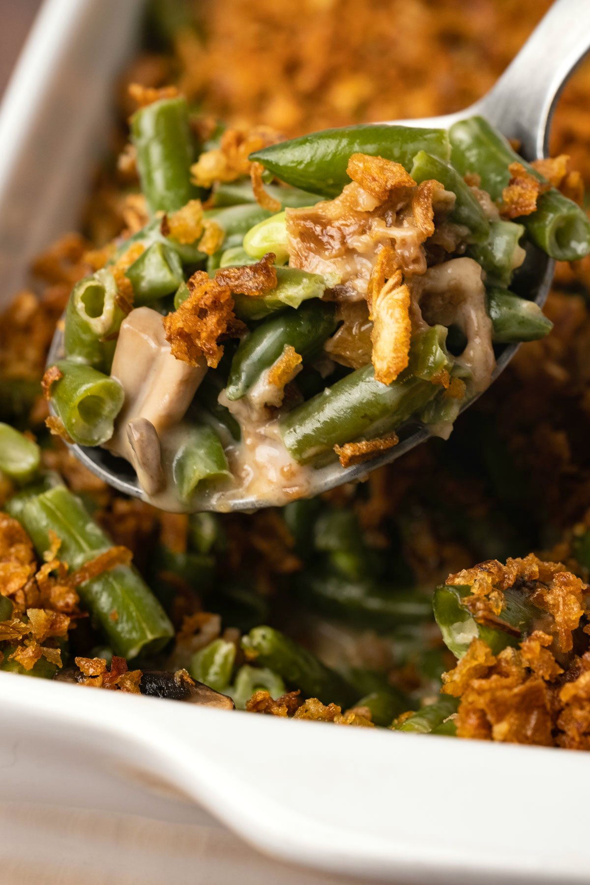 Vegan green bean casserole in a white dish with a serving spoon. 
