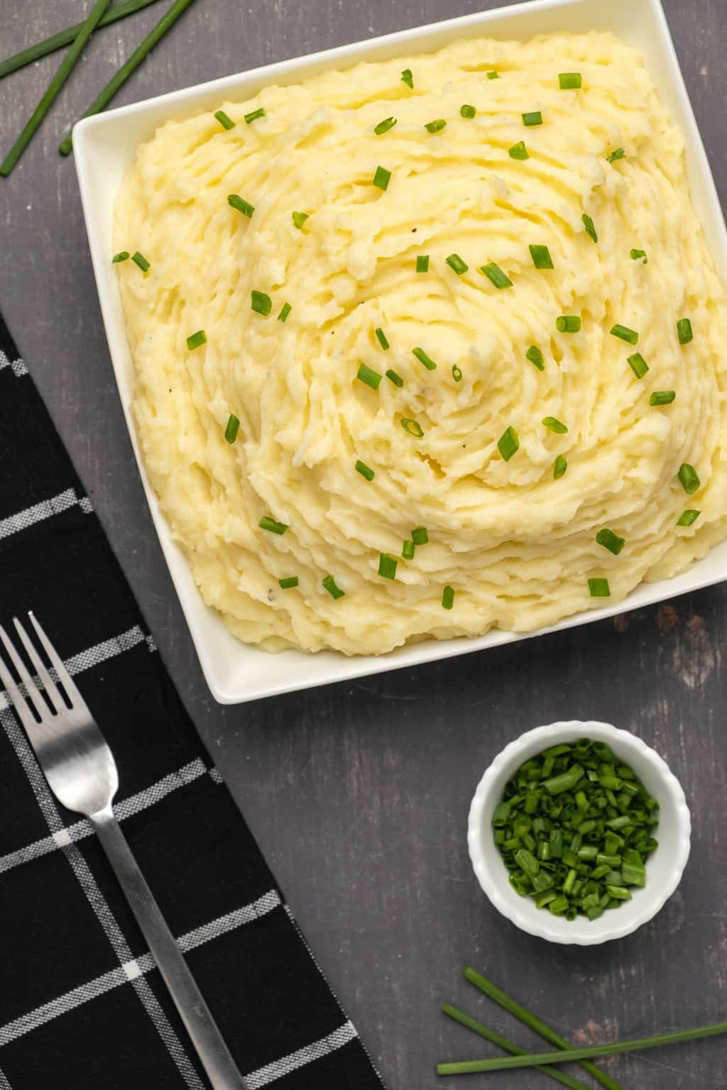 Vegan mashed potatoes topped with chopped chives in a white square dish. 
