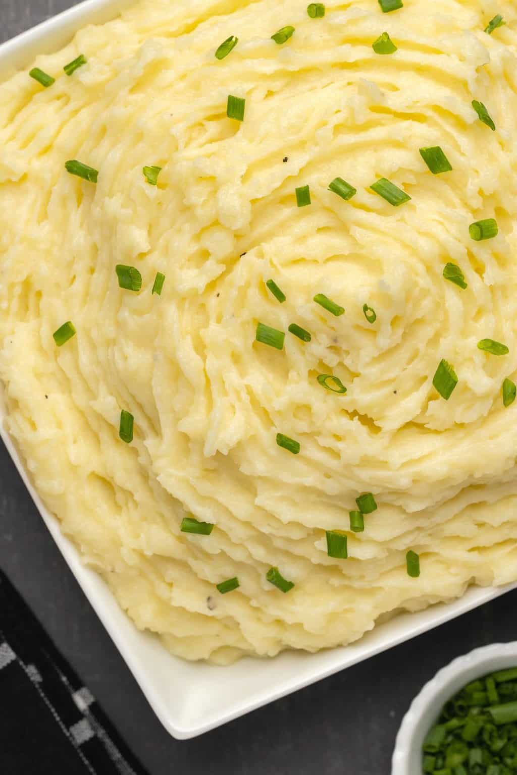 Vegan mashed potatoes topped with chopped chives in a white dish. 