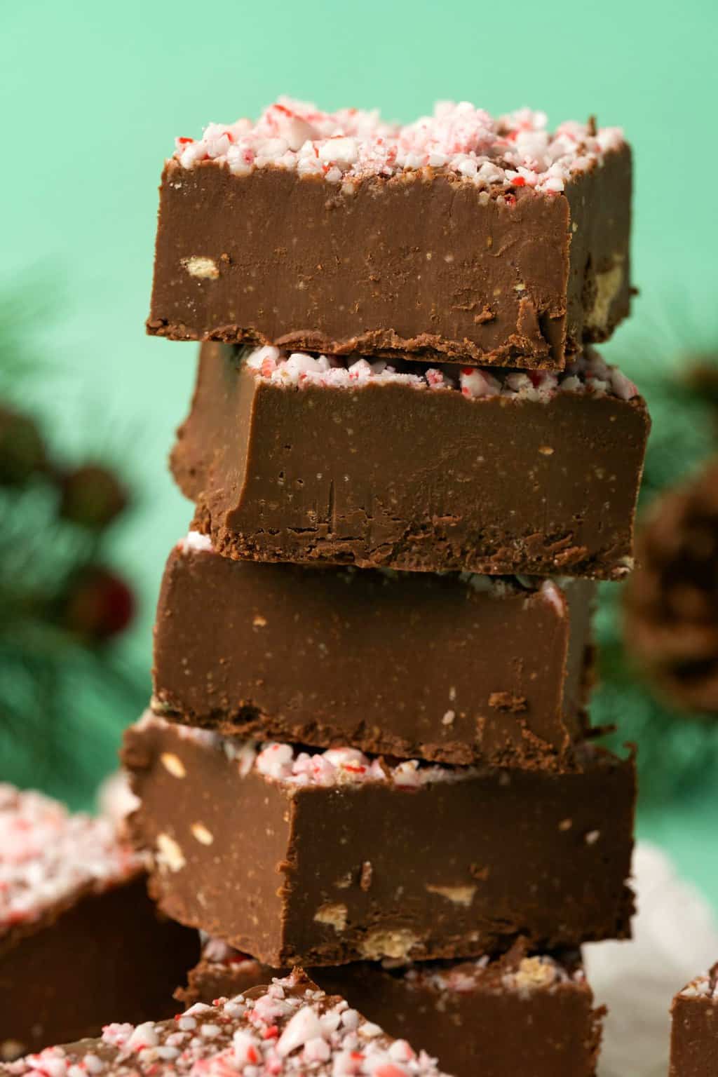 Vegan peppermint fudge topped with crushed candy canes in a stack. 