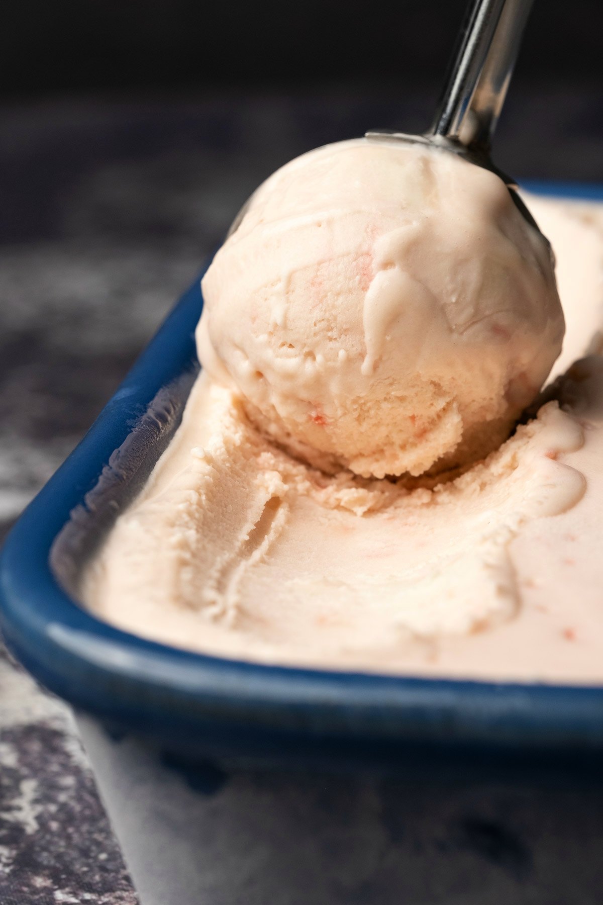 Vegan peppermint ice cream in a blue ceramic dish with an ice cream scoop. 