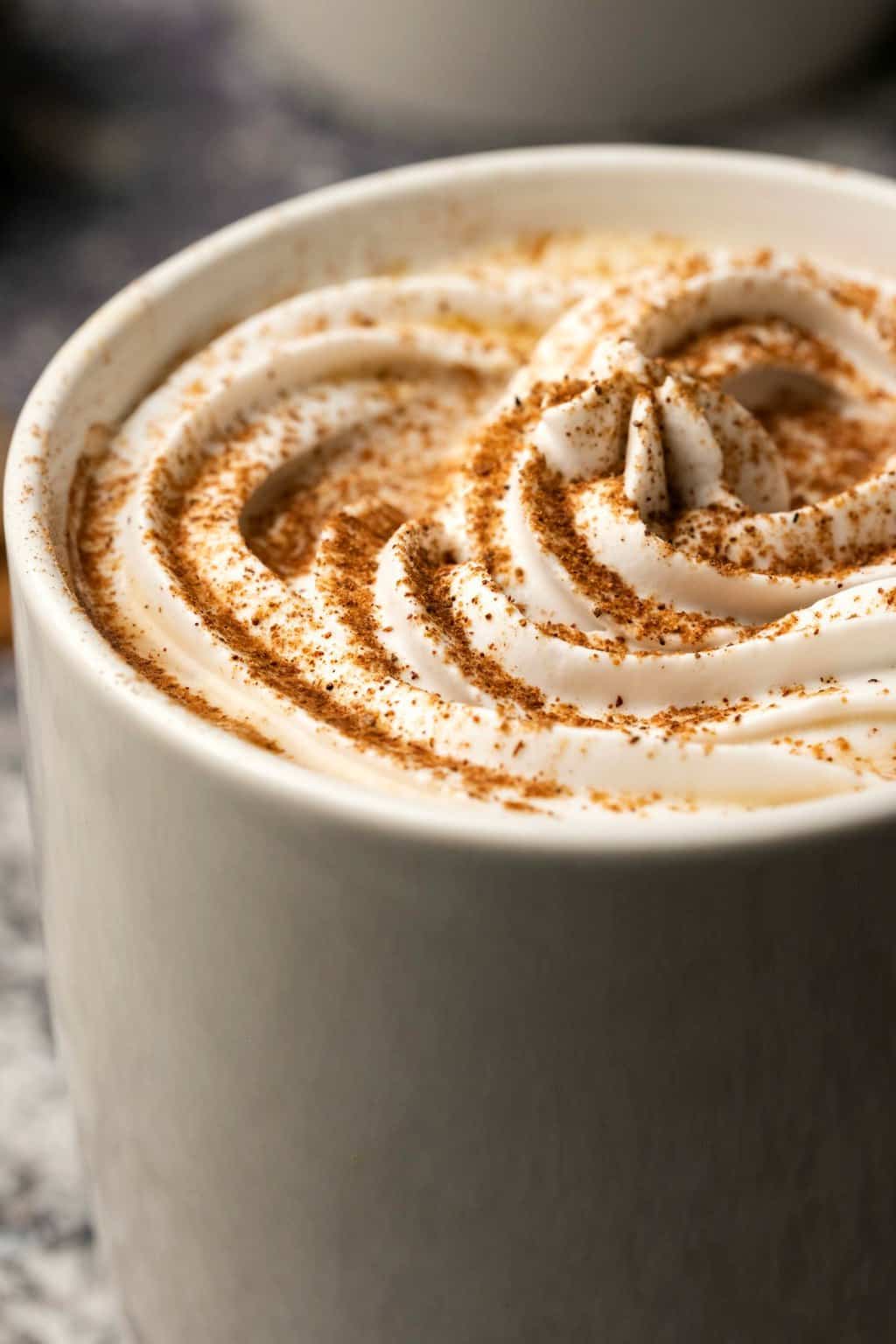 Vegan pumpkin spice latte topped with whipped cream and a sprinkle of pumpkin pie spice in a white mug. 
