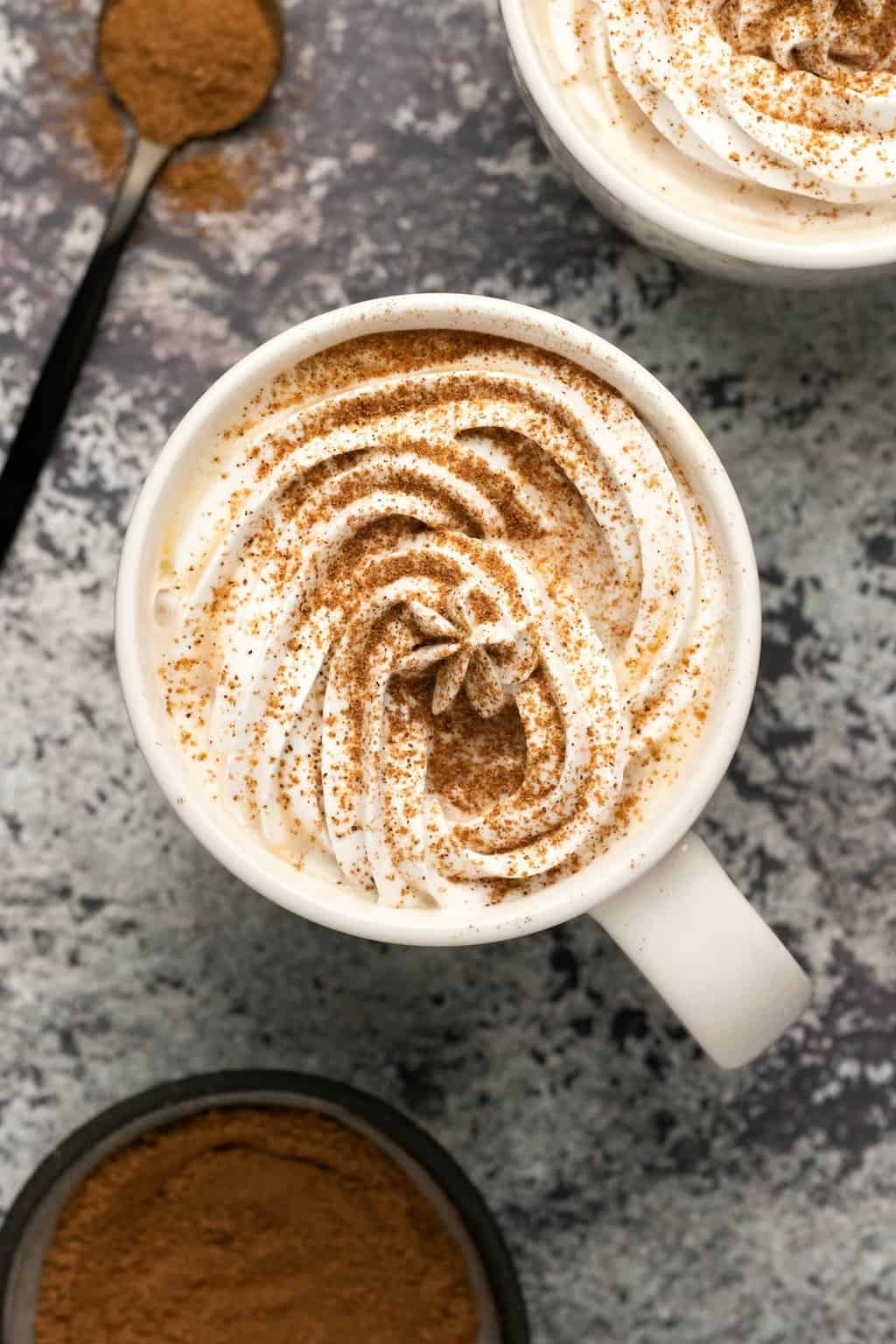 Vegan pumpkin spice latte topped with vegan whipped cream and pumpkin pie spice in a white mug. 