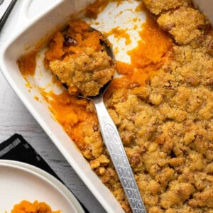 Vegan sweet potato casserole in a white dish with a serving spoon.