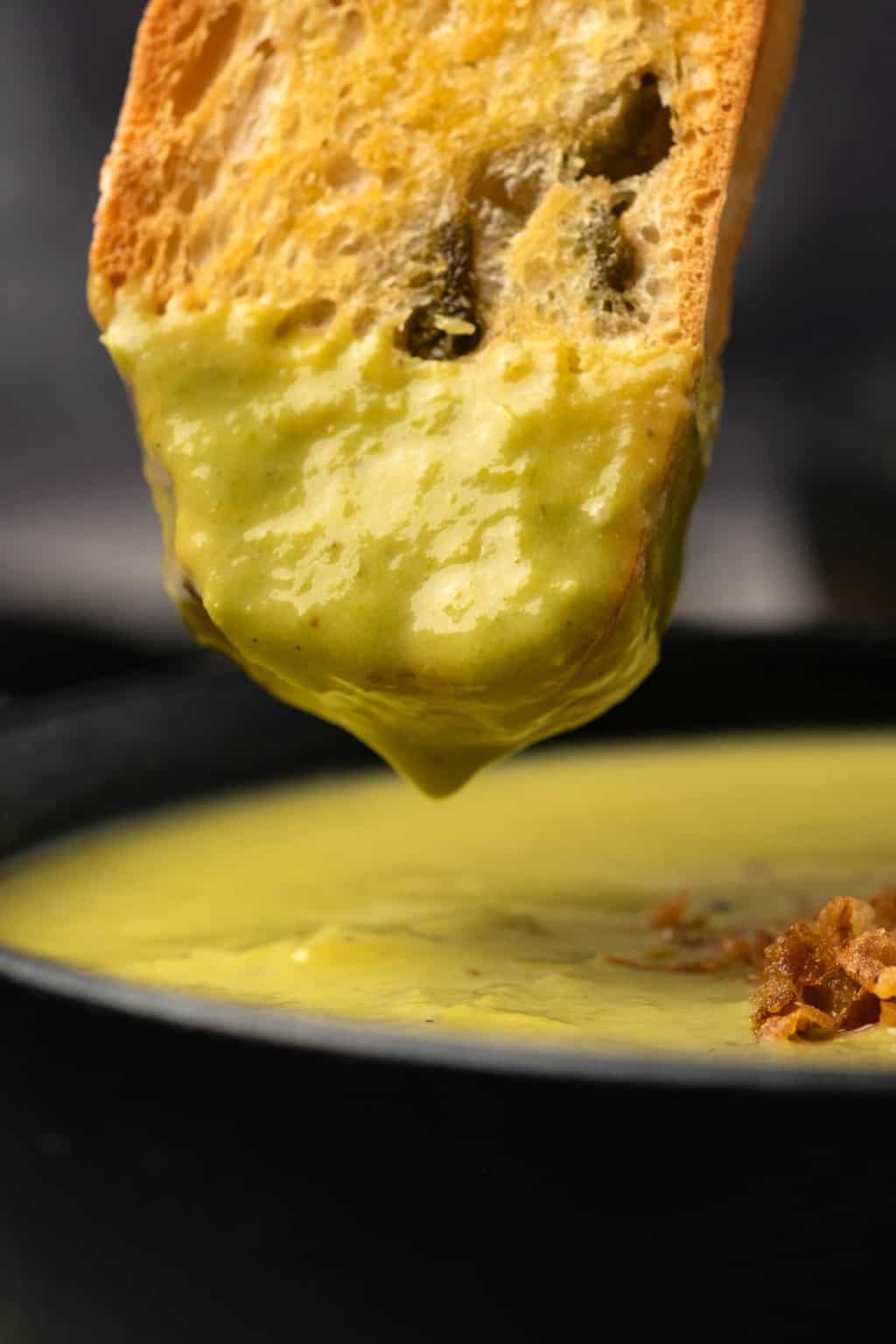 Toasted bread dipping into a bowl of asparagus soup. 
